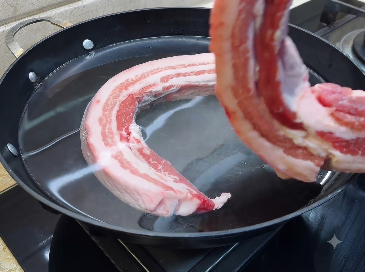 Un morceau de poitrine de porc cru plongé dans une grande casserole remplie deau froide.