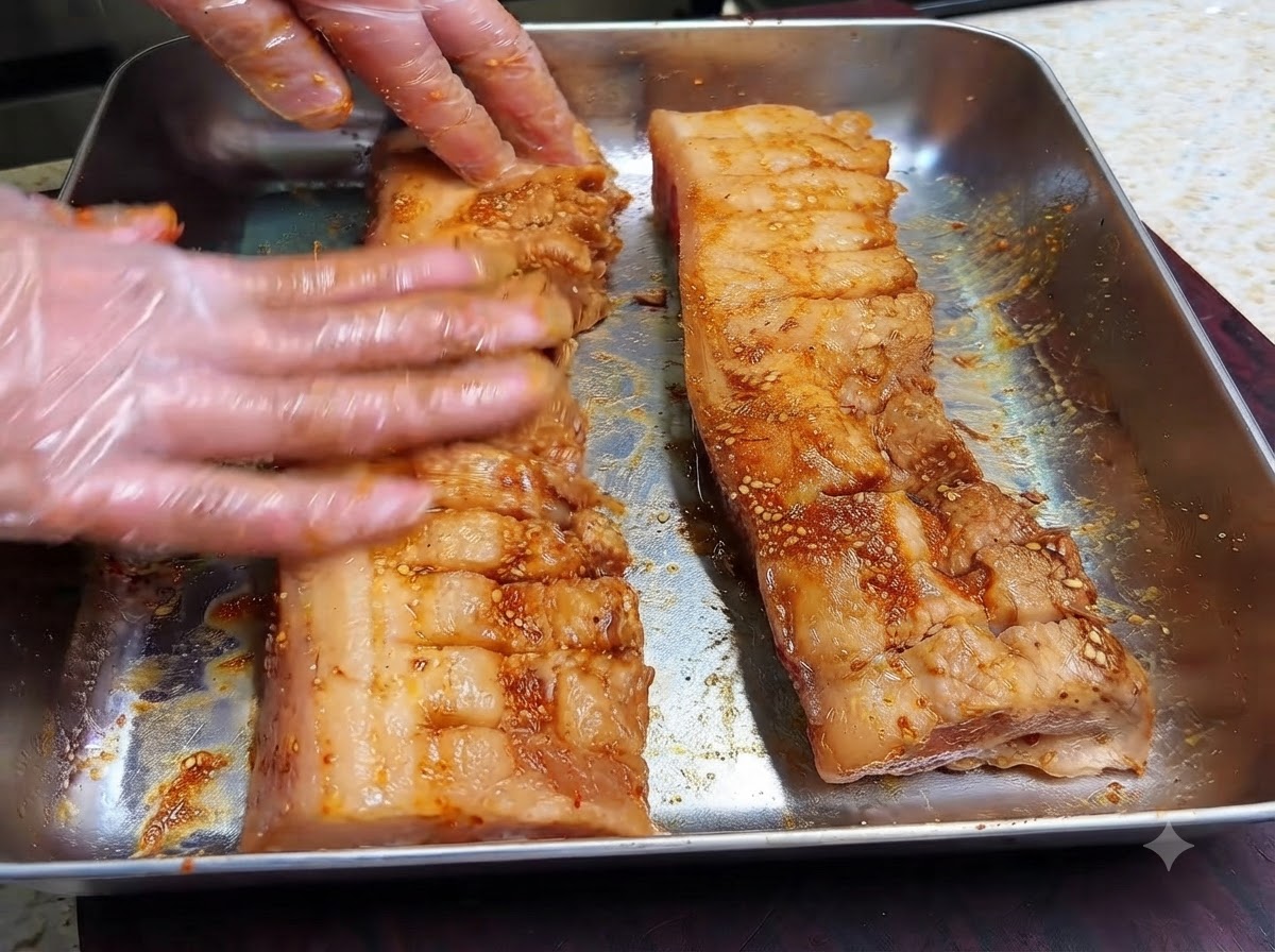Des mains gantées massant la marinade foncée et les épices sèches dans la surface quadrillée de deux lanières de poitrine de porc.