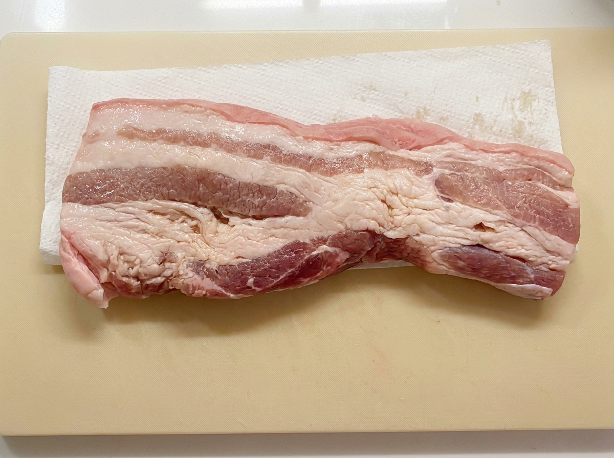 Une tranche de poitrine de porc posée à plat sur du papier absorbant sur une planche à découper en train dêtre séchée.