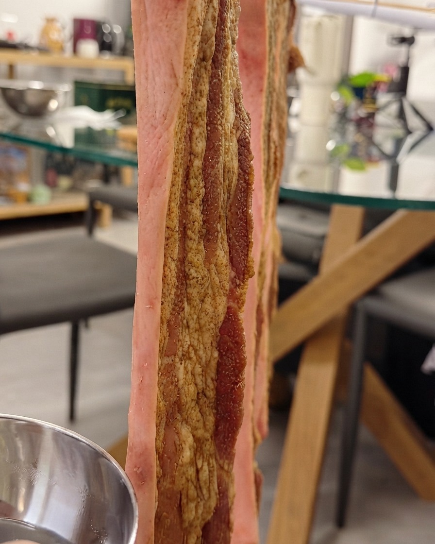 Poitrine de porc suspendue verticalement sur une grille pendant quelle est badigeonnée deau croustillante sur la peau.