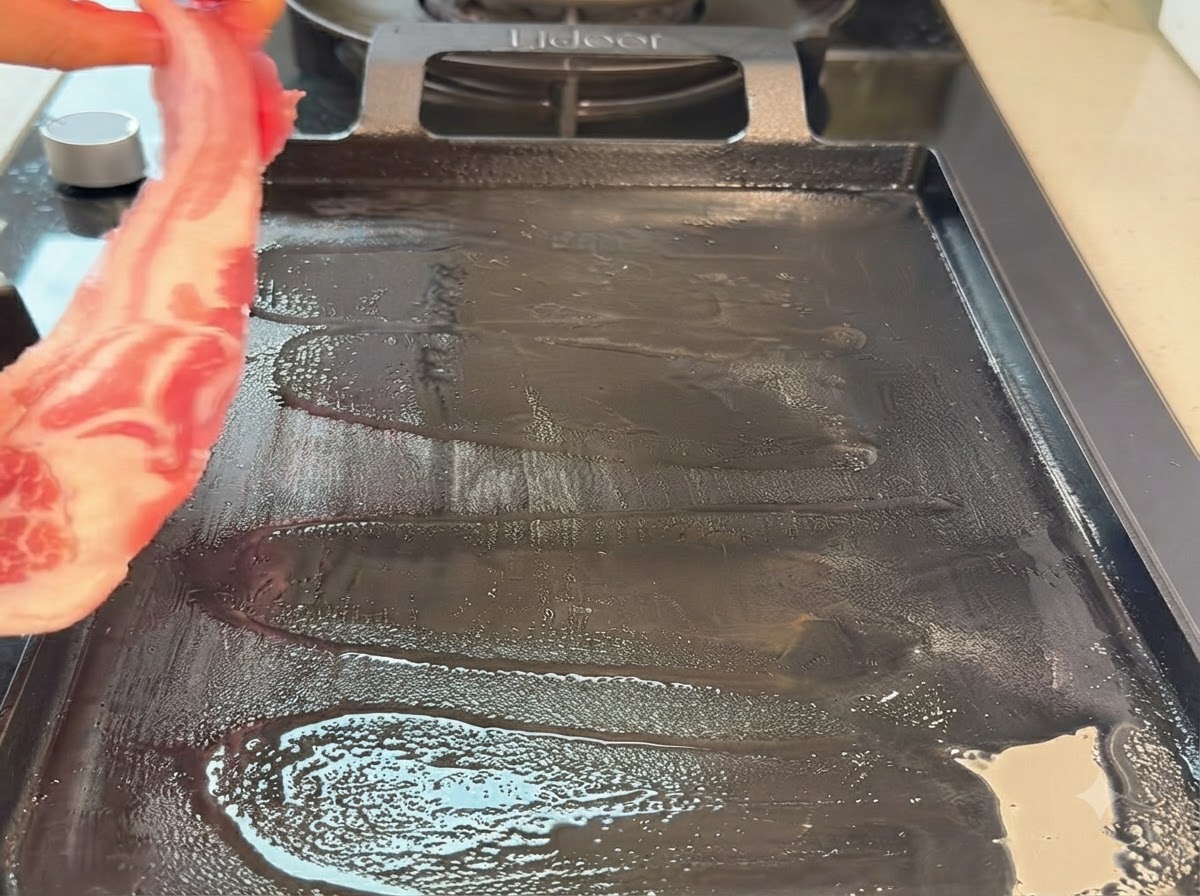 Une lanière de poitrine de porc crue placée sur une poêle de type teppanyaki chaude.