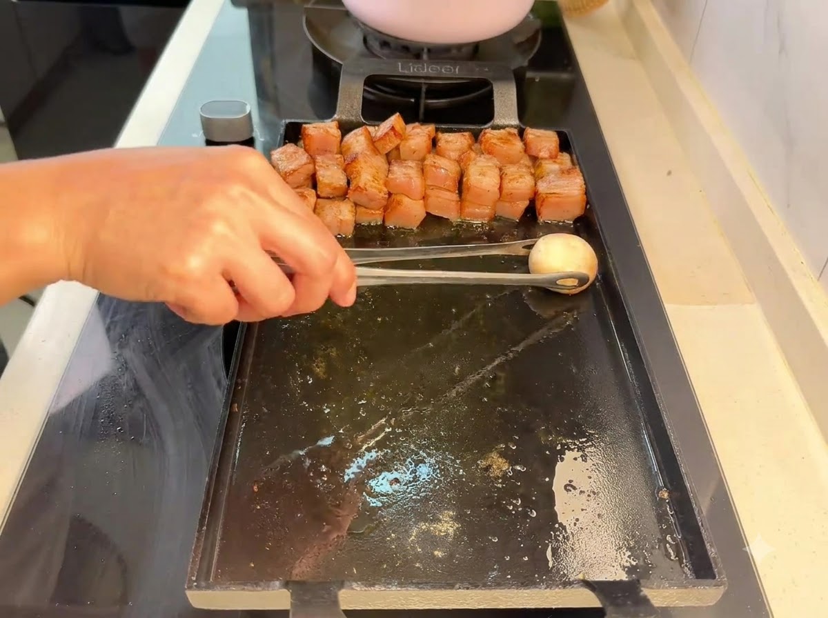 Un champignon de Paris déposé à laide de pinces sur le gril à côté des morceaux de porc grillés.