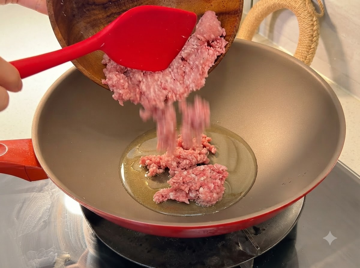 Du porc haché frais versé dun bol en bois dans un wok rouge chauffé avec de lhuile.