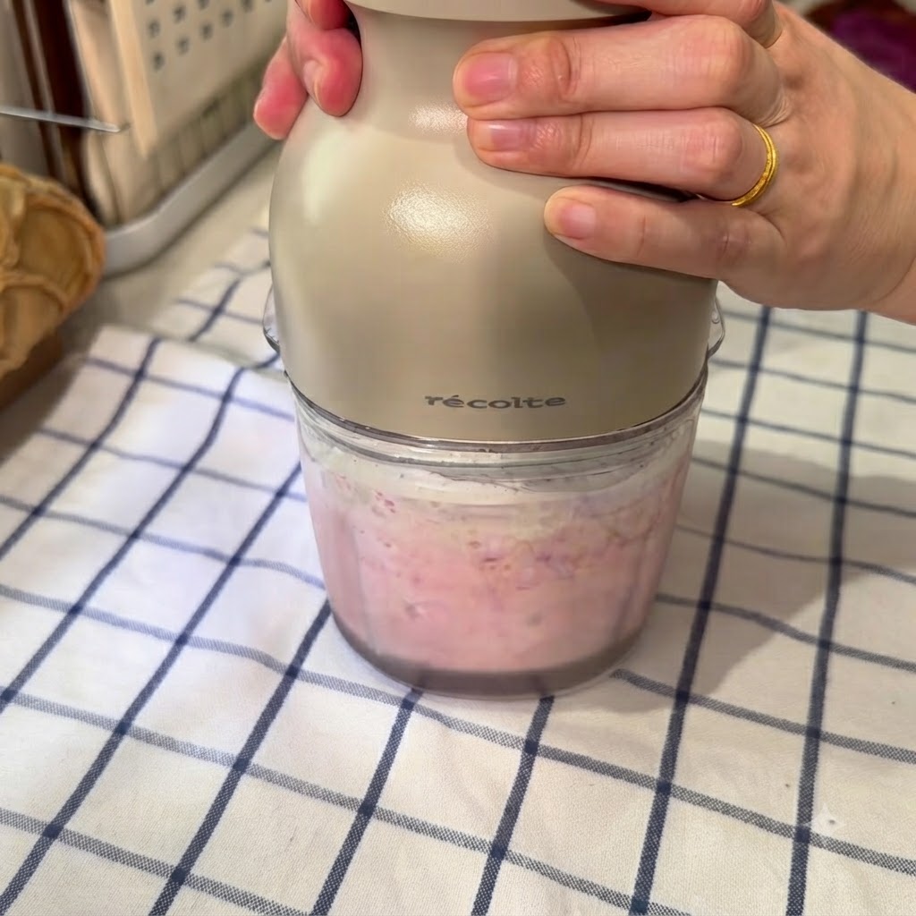 Un robot culinaire mixant un mélange rose de pastèque congelée, deau glacée et de lait concentré.