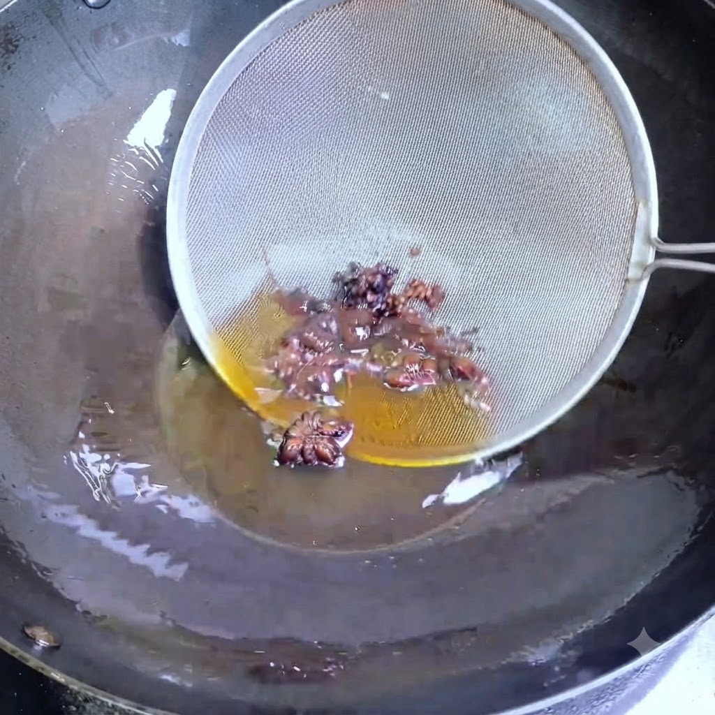 Une écumoire en fil de fer récupérant de lanis étoilé et des baies de Sichuan sombres dans de lhuile chaude dans un wok.