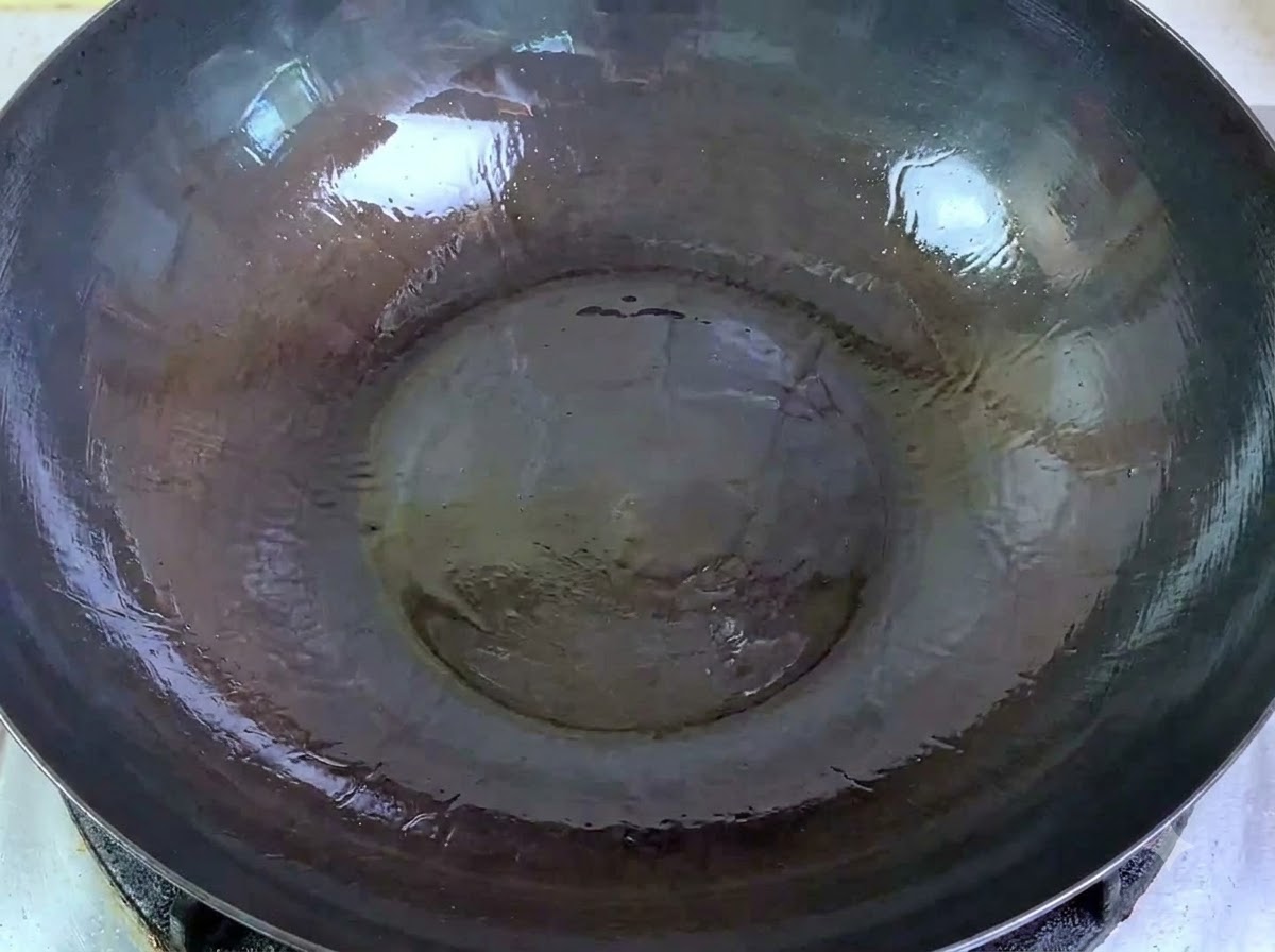 Du porc haché cru versé dun bol dans un grand wok contenant de lhuile chaude.