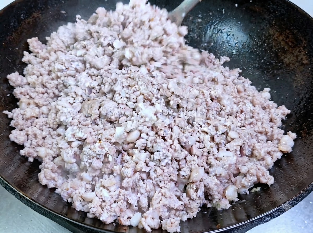 Du porc haché en train de cuire et de devenir opaque dans un wok culotté.