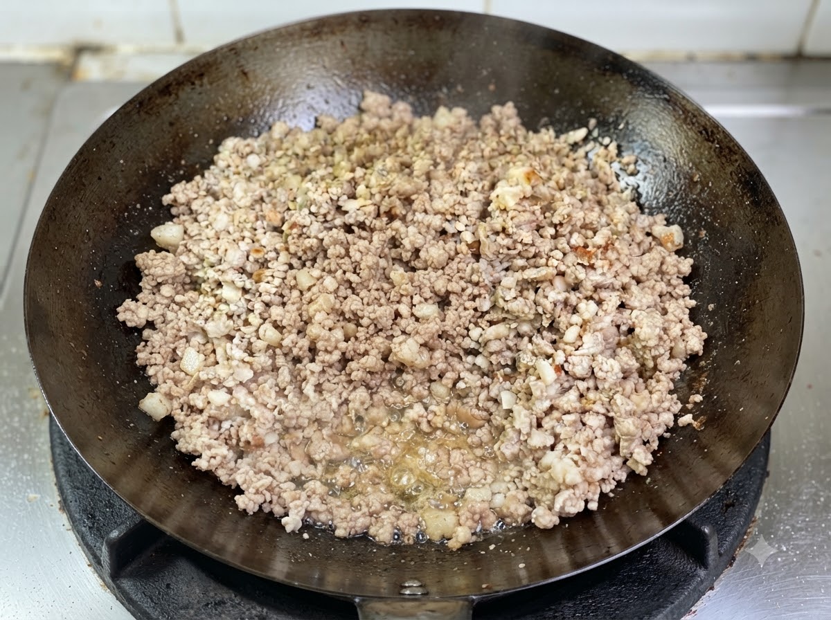 Du porc haché dorant dans un wok avec de lhuile fondue visible qui bouillonne à la base.