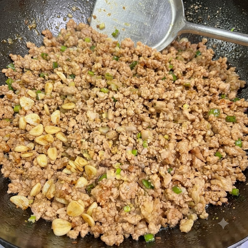 Du porc haché cuit mélangé à des ciboules et de lail en train dêtre remué dans un wok avec une spatule.