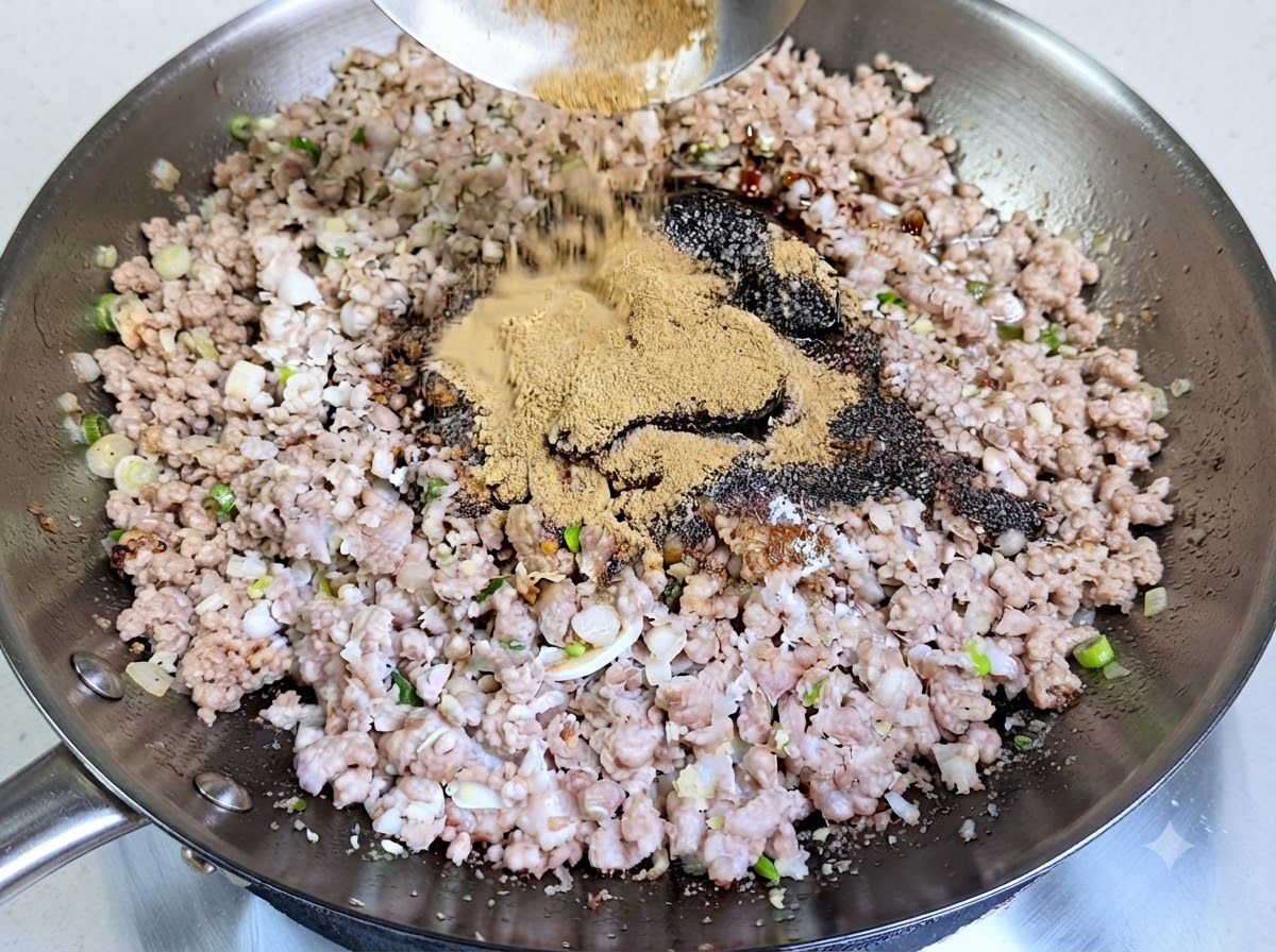 Un tas généreux de poudre dépices brun clair versé dune louche dans le wok sur le porc haché assaisonné.