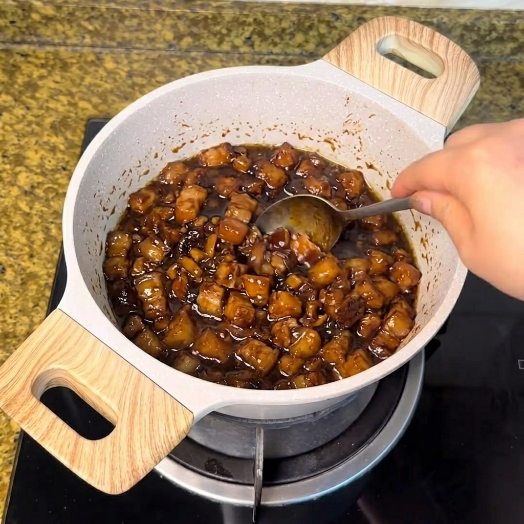 Du sucre blanc remué avec une cuillère dans la sauce de viande sombre qui mijote.