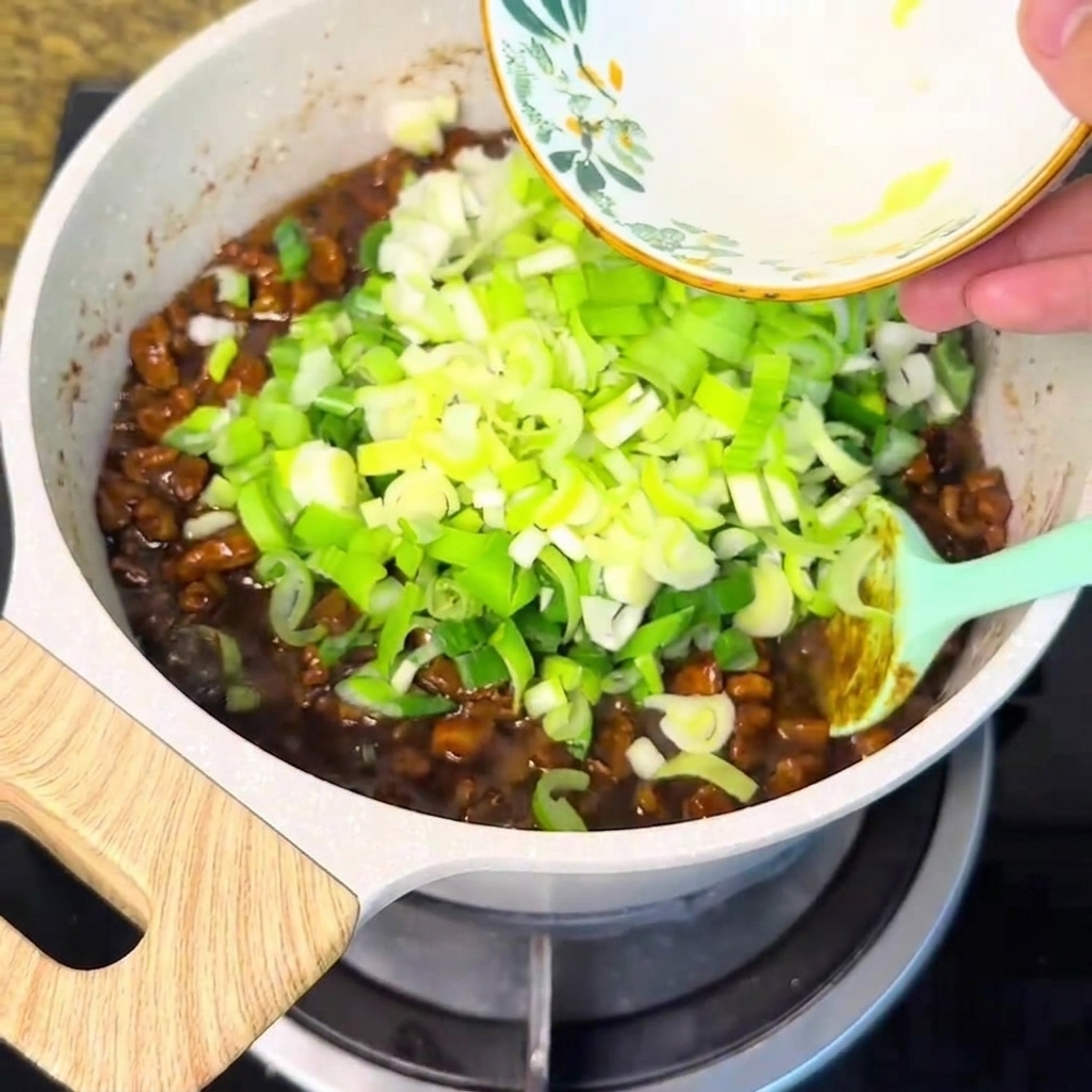 Des oignons verts hachés versés depuis un bol dans la sauce de viande bouillonnante.