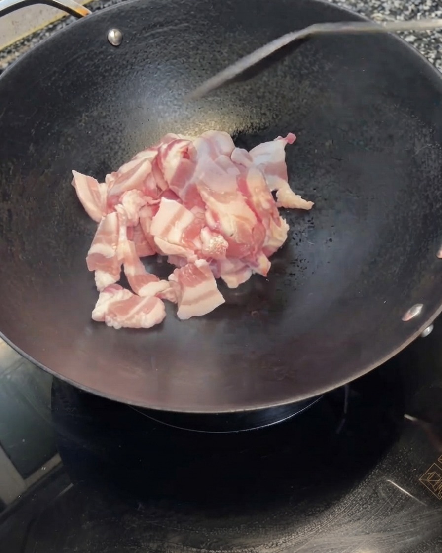 Tranches de poitrine de porc versées dun bol blanc dans un wok noir chaud.