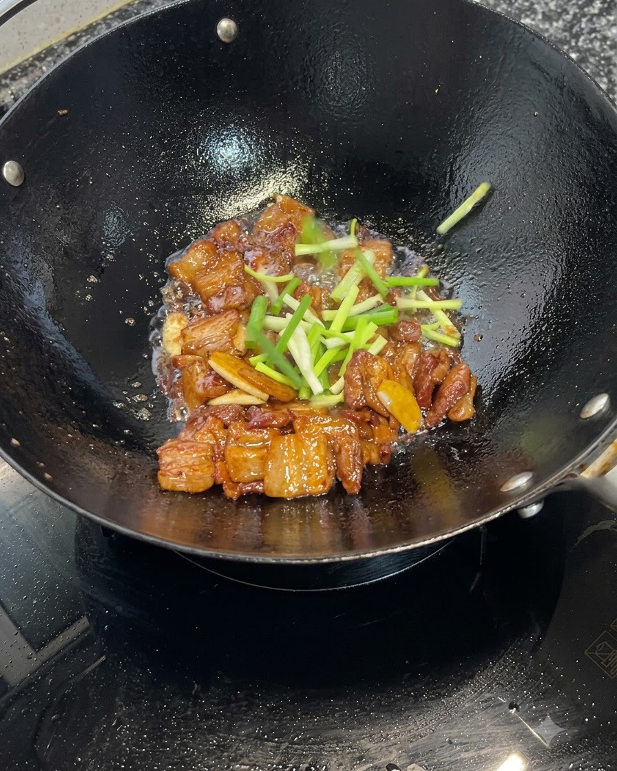 Morceaux doignons verts frais parsemés sur des morceaux de poitrine de porc caramélisés cuisant dans un wok.