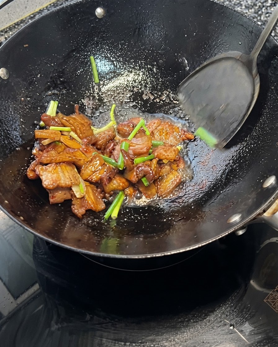 Une spatule mélangeant de la poitrine de porc et des oignons verts à lintérieur dun wok chaud.