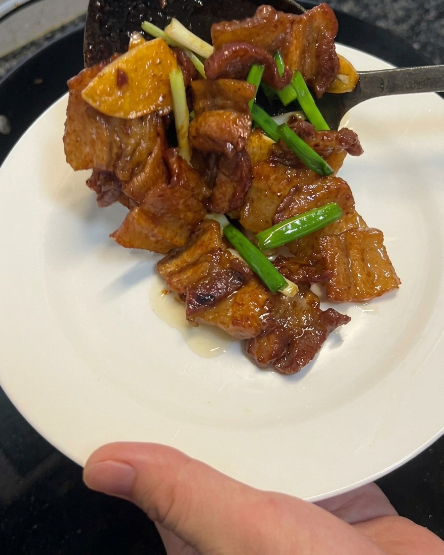 Poitrine de porc à la sauce soja cuite retirée du wok à laide dune spatule vers une assiette blanche propre.