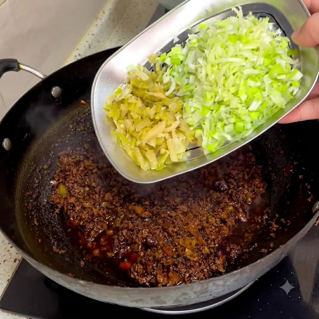 Des légumes moutarde conservés et des oignons verts hachés glissant dun plateau en métal dans une sauce de viande sombre dans un wok.