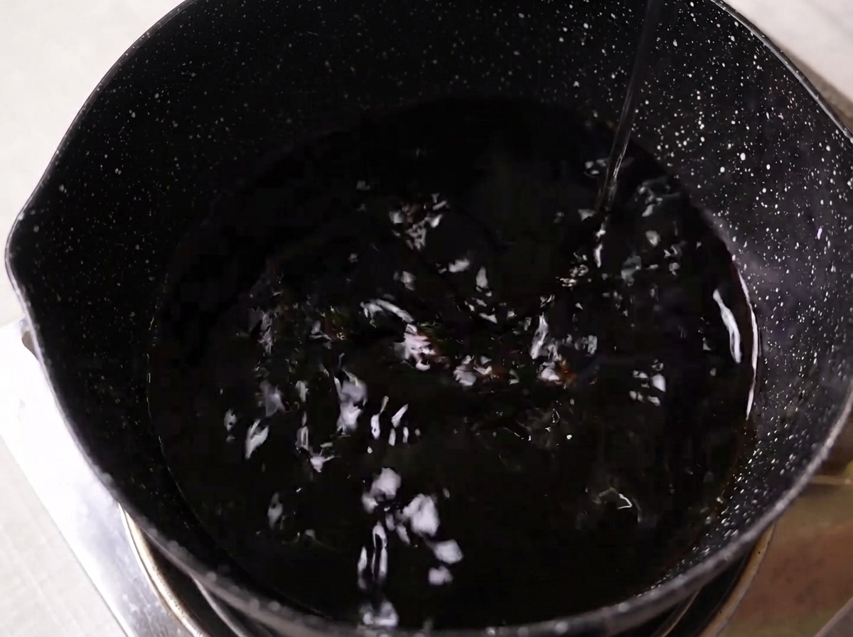 Sauce soja, mirin, saké et sucre blanc mélangés dans une casserole sombre sur une cuisinière.