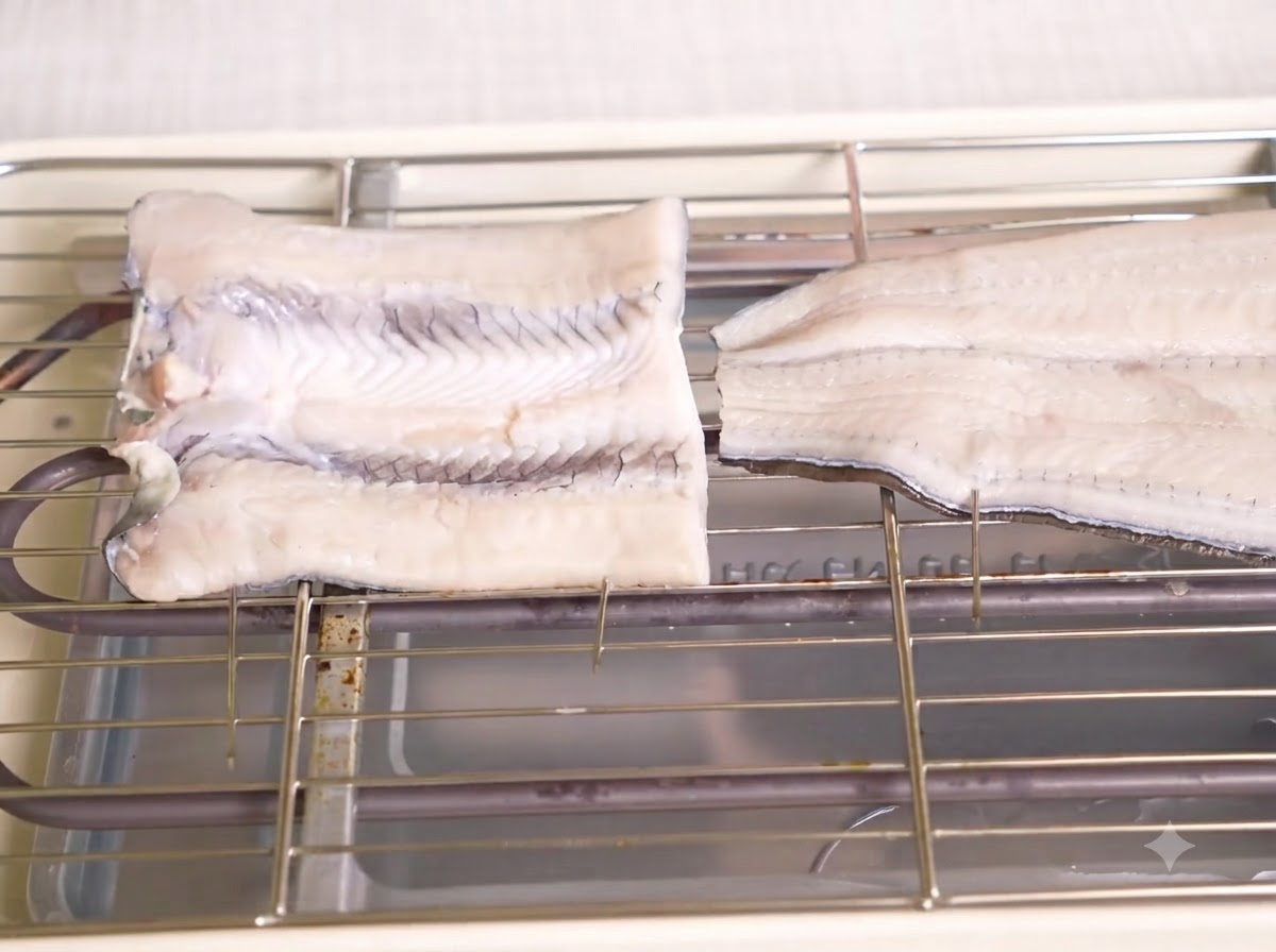 Deux morceaux danguille crue en papillon sur des brochettes, placés sur la grille métallique dun gril électrique.
