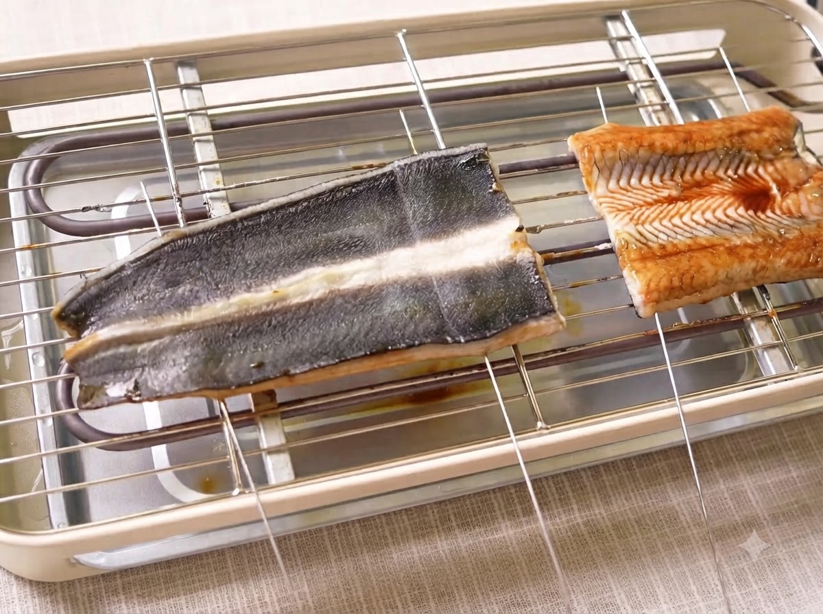 Des filets danguille en cours de cuisson sur un gril électrique, traversés par des brochettes en métal.