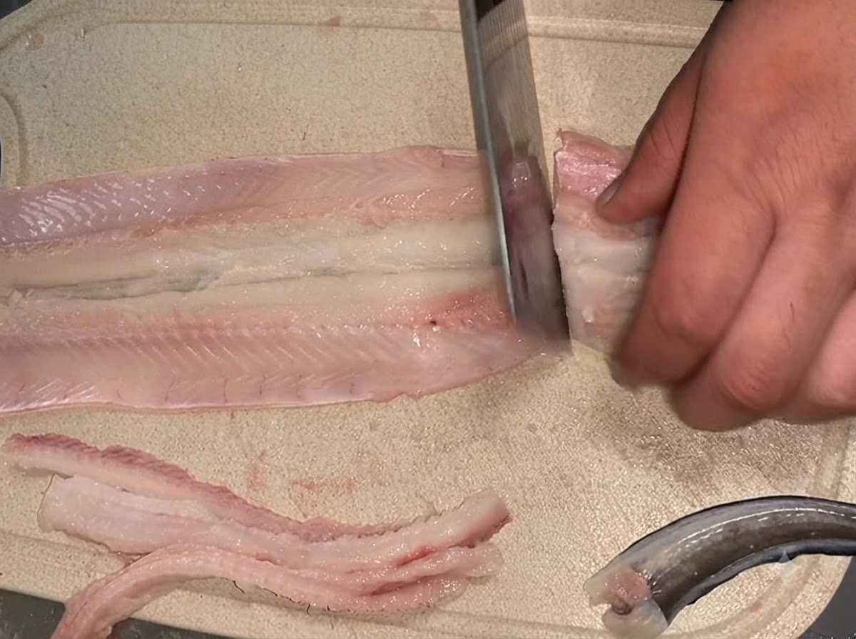 Couteau coupant un filet danguille crue désarêtée en deux sections égales sur une planche à découper.