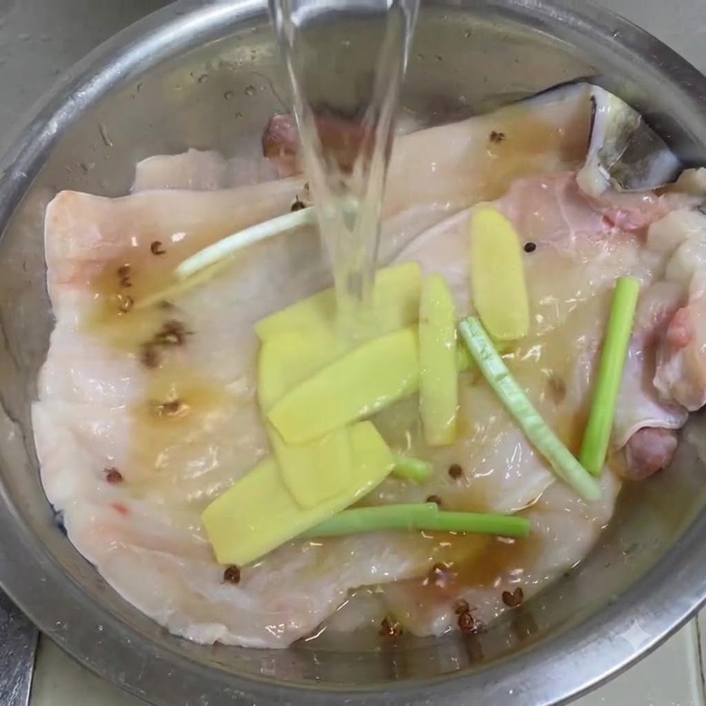 De leau claire versée dans un bol en métal contenant les filets danguille, le gingembre, la ciboule et le poivre du Sichuan.
