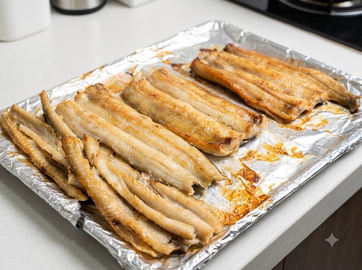 Gros plan de filets danguille partiellement cuits badigeonnés dhuile sur la plaque de cuisson.