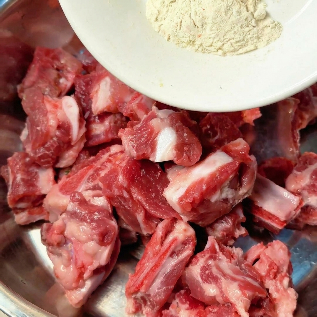 Épices et condiments liquides versés directement sur les côtes de porc crues dans un bol mélangeur en métal.