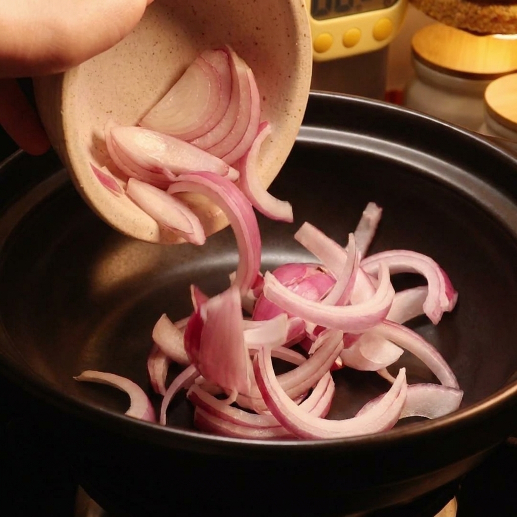 Des tranches doignon rouge versées dun bol en céramique dans une cocotte noire.