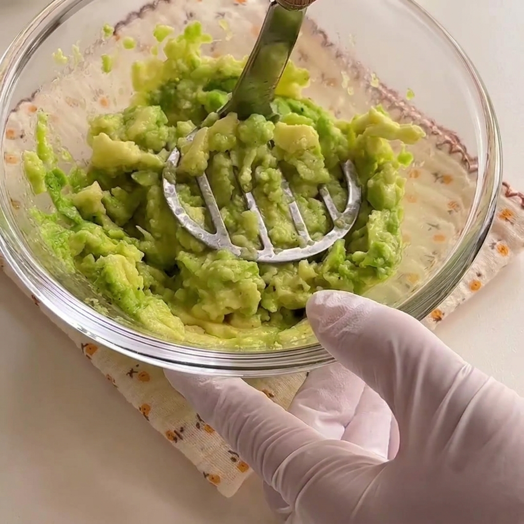 Des moitiés davocat réduites en une pâte vert vif à lintérieur dun bol en verre avec un presse-purée.