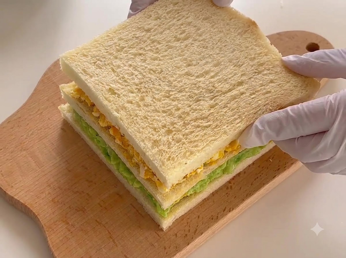 Le sandwich à trois couches entièrement assemblé reposant sur une planche à découper, prêt à être découpé.