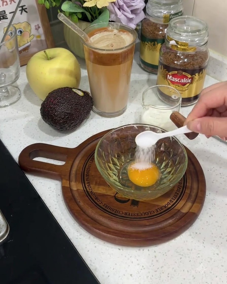 Une petite cuillère blanche ajoutant du sel directement sur le jaune dun œuf cru dans un bol en verre.