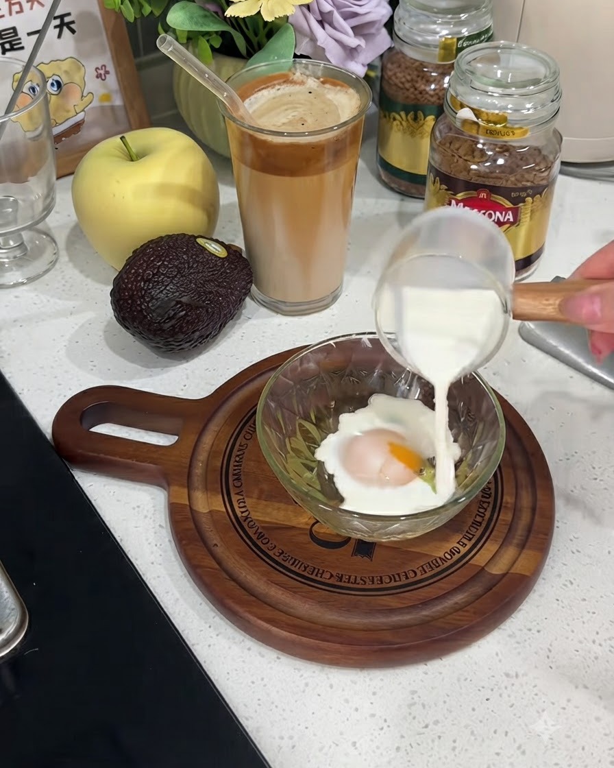 Du lait versé dune petite pichet en verre dans un bol contenant un œuf cassé.