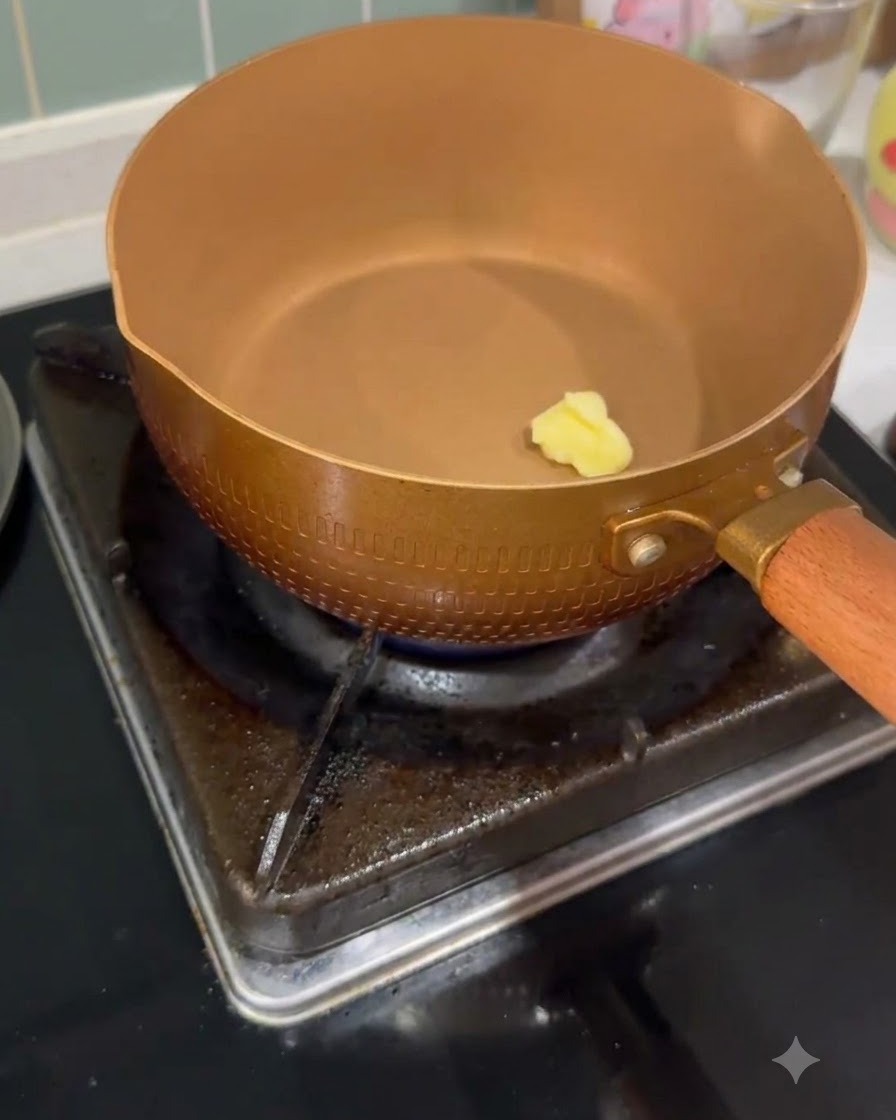 Une petite noisette de beurre en train de fondre à lintérieur dune casserole couleur cuivre chauffée sur un brûleur à gaz.