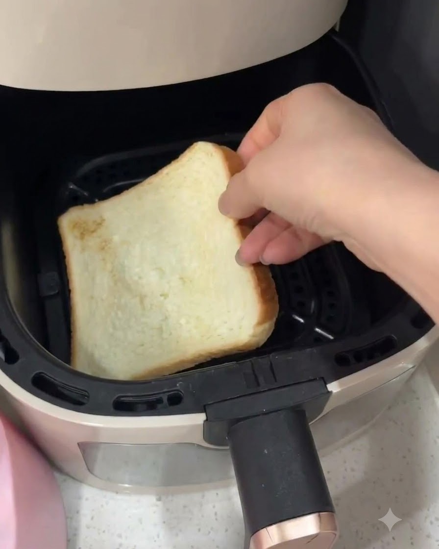 Une main plaçant une tranche de pain de mie blanc à lintérieur dun panier de friteuse à air.
