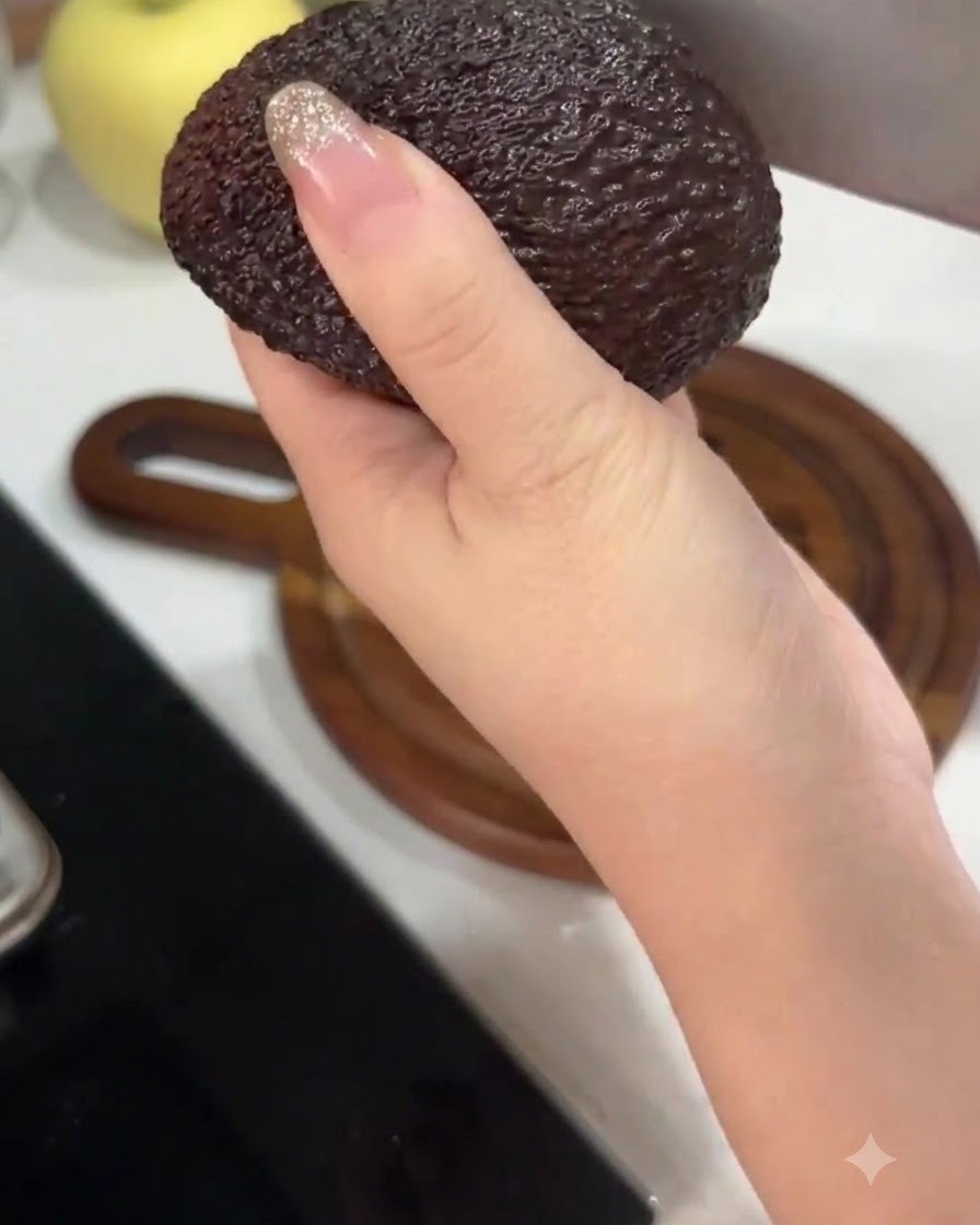 Une main tenant un avocat tout en le coupant en deux avec un grand couteau de cuisine.
