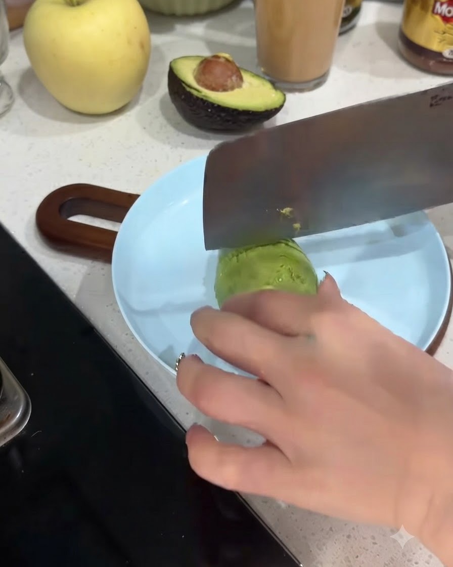 Une moitié davocat en train dêtre coupée en morceaux fins sur une assiette bleu clair.