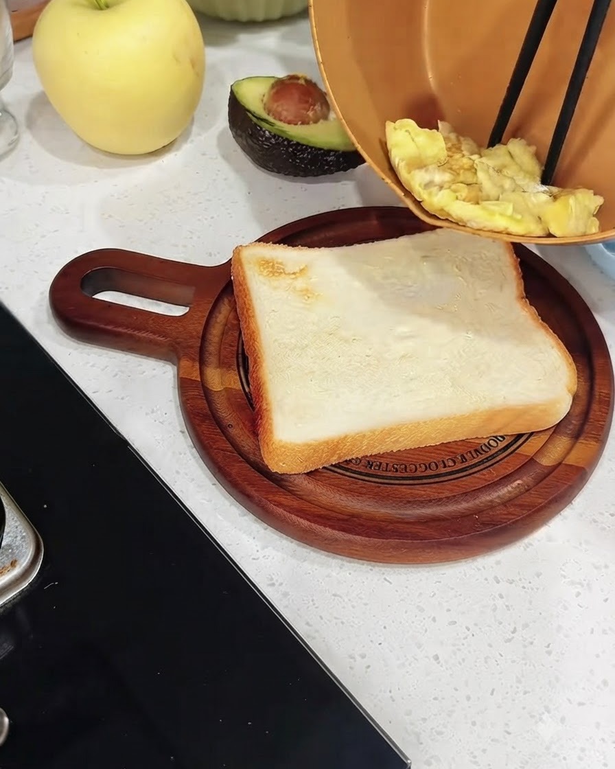 Des œufs brouillés cuits en train dêtre transférés dune poêle en cuivre sur une tranche de pain blanc grillé sur une planche en bois.
