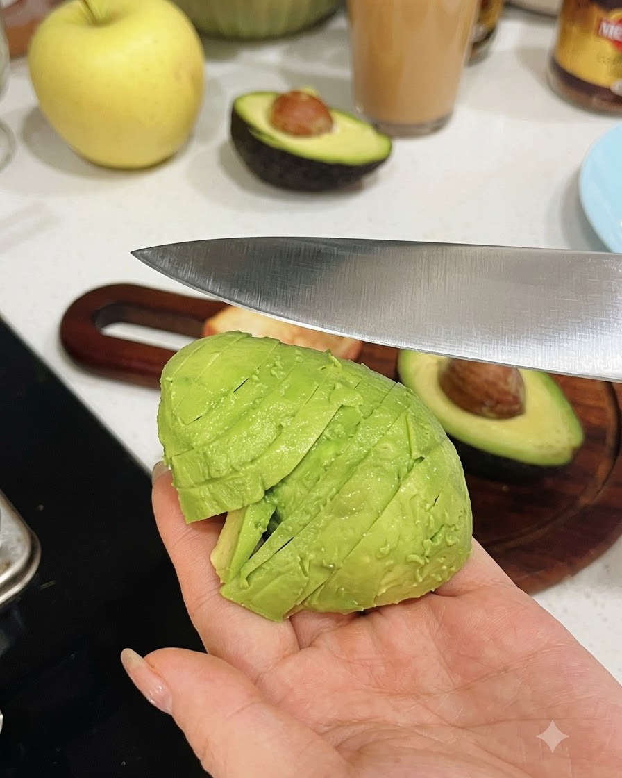 Une main tenant une moitié davocat pelé tandis quun couteau de cuisine le tranche en morceaux uniformes.