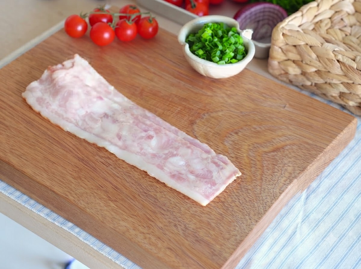 Une seule tranche de bacon cru posée sur une planche à découper en bois prête à être tranchée.