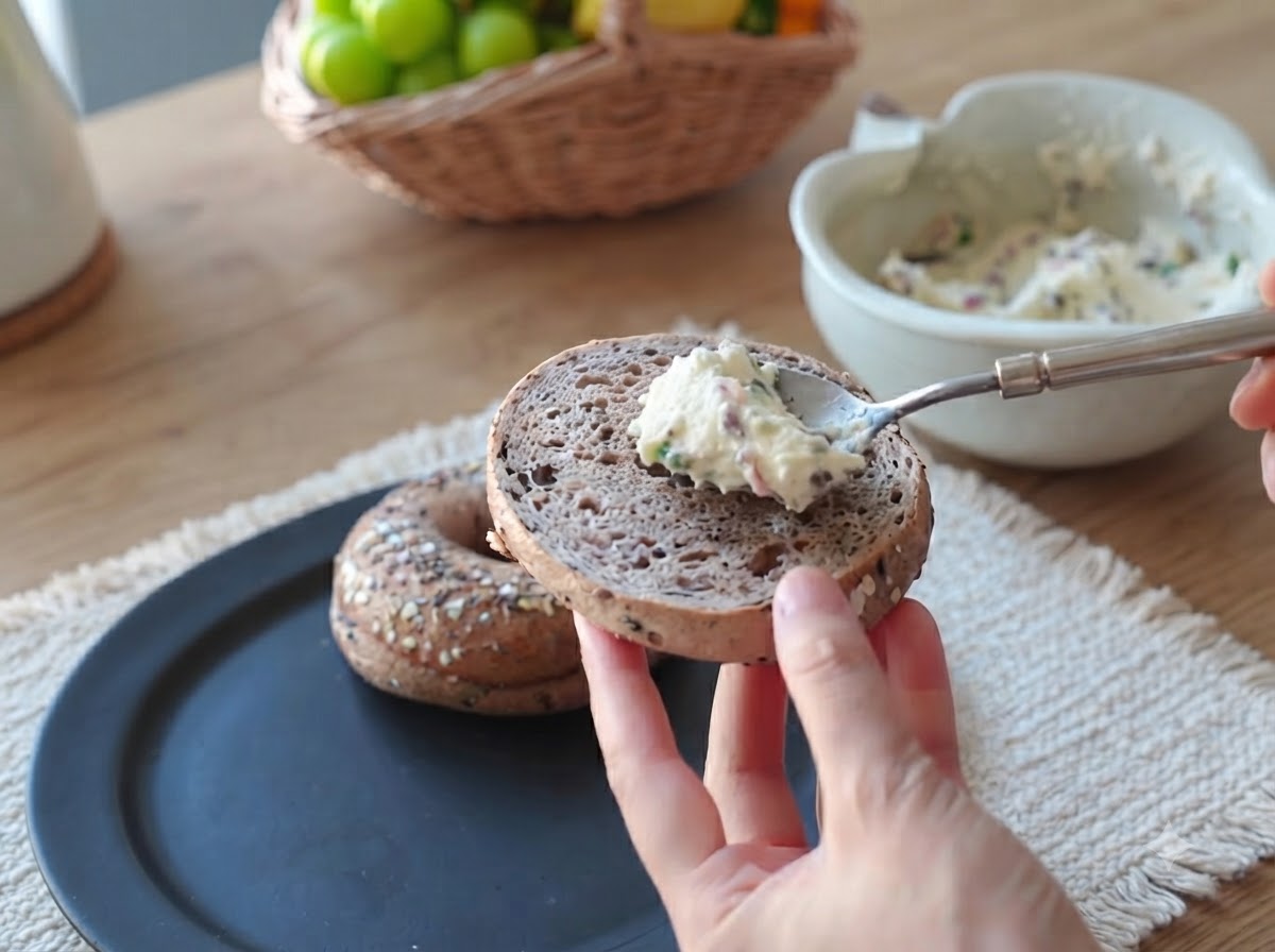 Une cuillerée de préparation crémeuse au bacon et à la ciboule étalée sur la surface dune moitié de bagel.