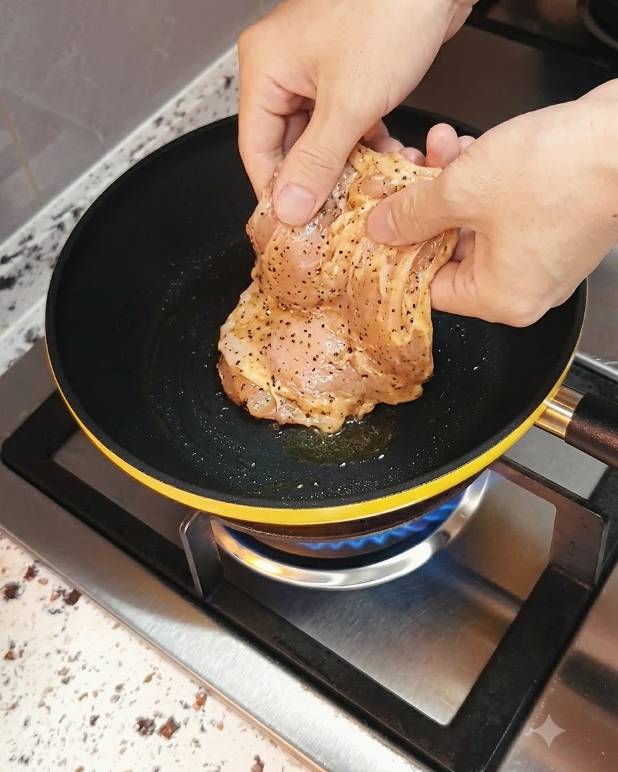 Une poitrine de poulet marinée placée dans une poêle chaude avec une flamme de gaz en dessous.