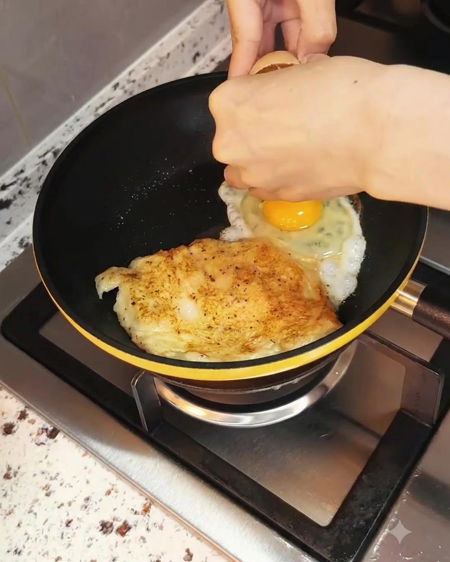 Un œuf cassé dans la poêle à côté du poulet en train de cuire.