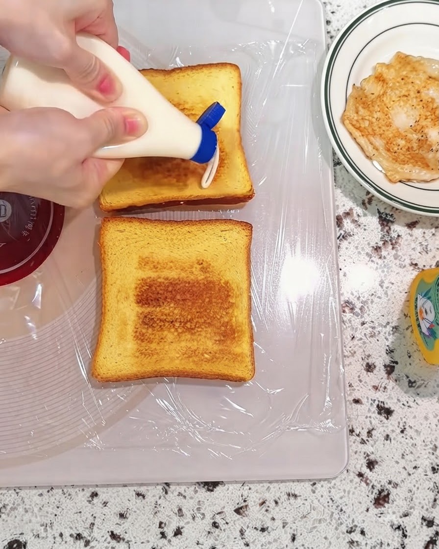De la mayonnaise pressée dune bouteille sur des tranches de pain grillé posées sur une planche à découper.