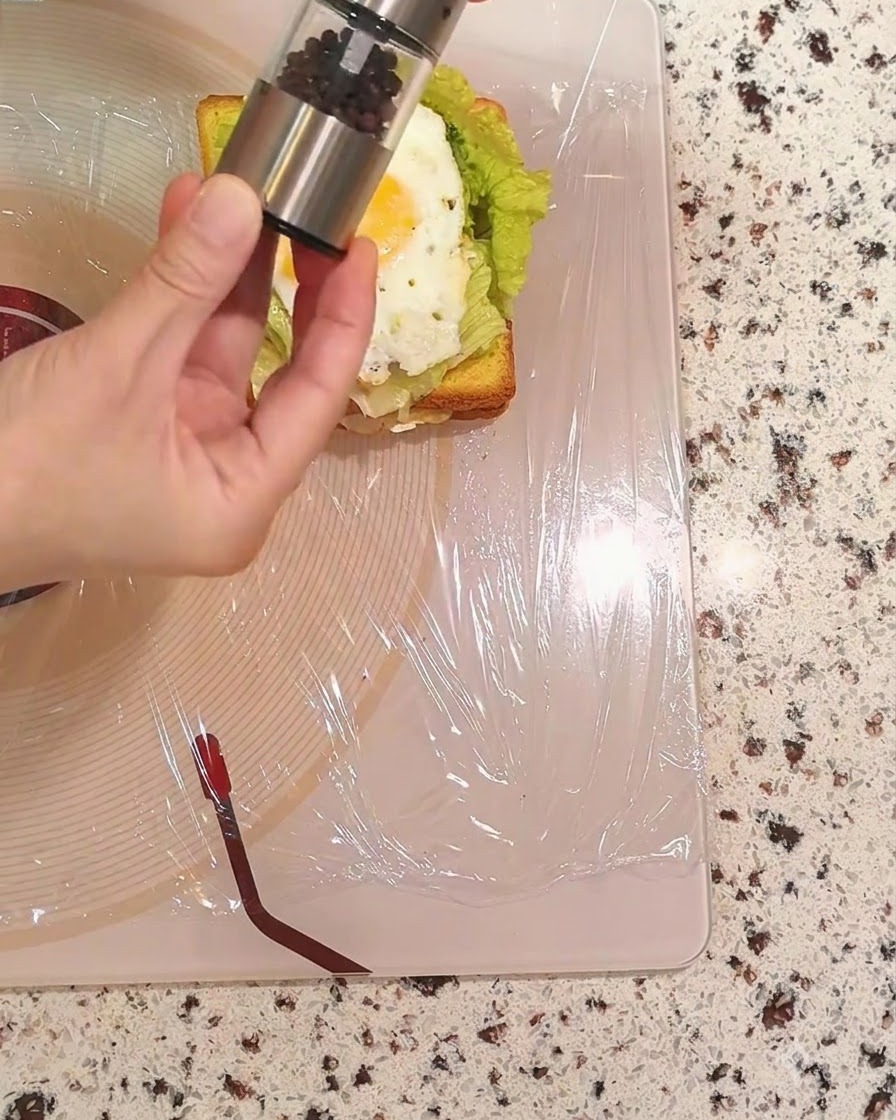 Une main tenant un moulin à poivre et saupoudrant du poivre noir sur lœuf frit.