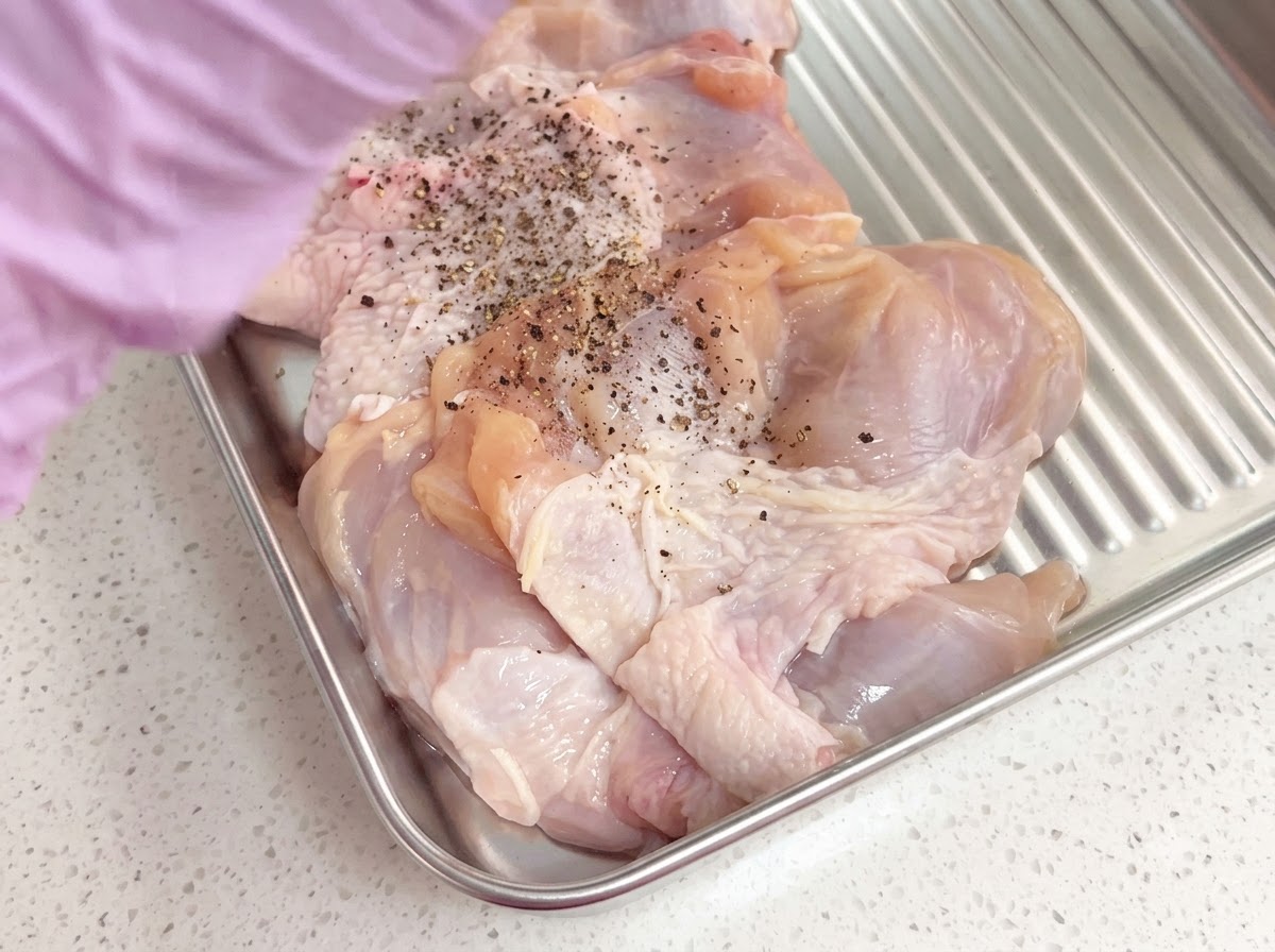 Des hauts de cuisse de poulet désossés assaisonnés de poivre noir fraîchement moulu dans un plateau en métal.