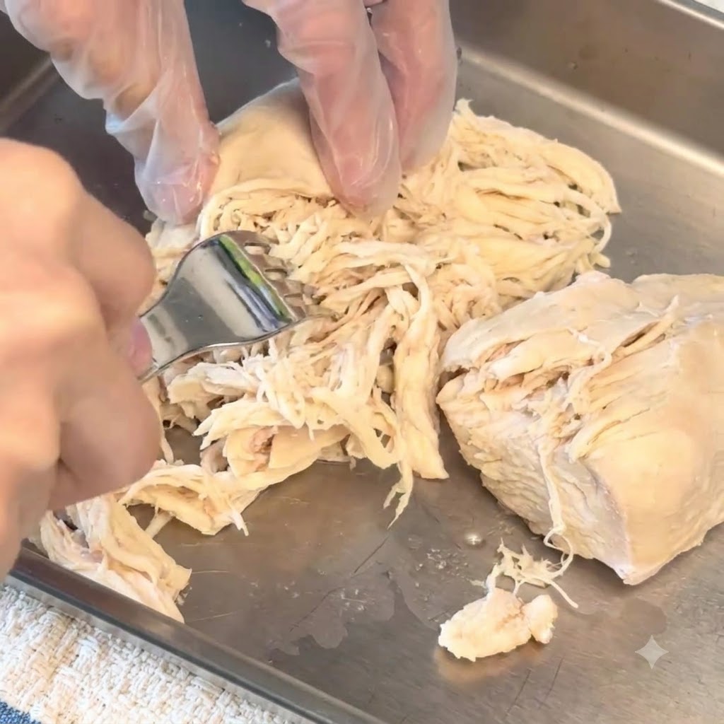 Un blanc de poulet cuit effiloché en petits morceaux sur un plateau à laide dune fourchette.