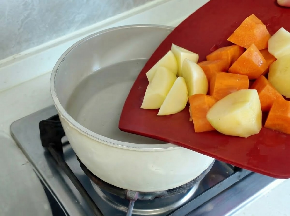 Morceaux de pommes de terre et de carottes bouillant dans une casserole sur un brûleur de cuisinière chaud.