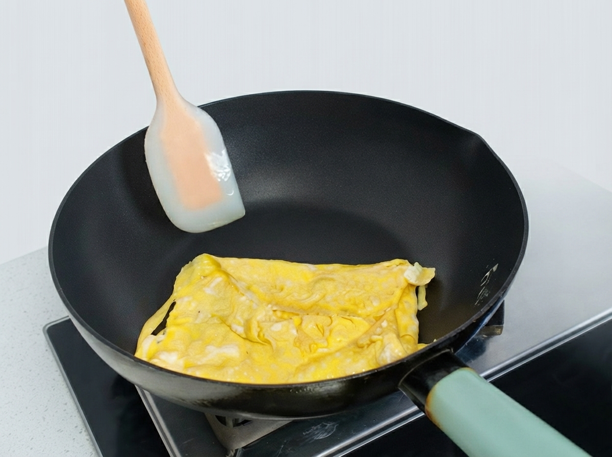 Omelette partiellement pliée dans une poêle façonnée à laide dune spatule en silicone.