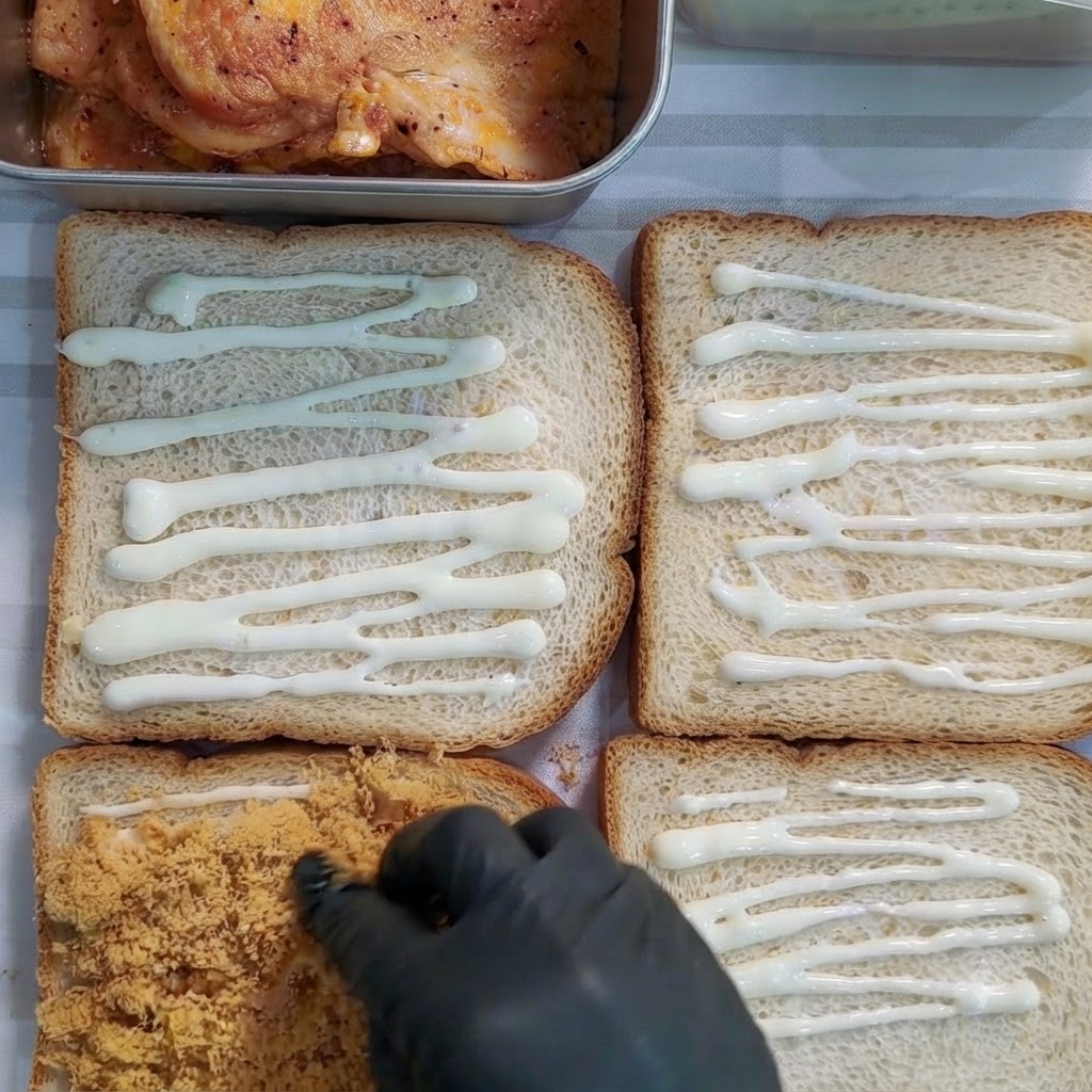 Main gantée répartissant du floss de porc doré sur une tranche de pain recouverte de sauce.